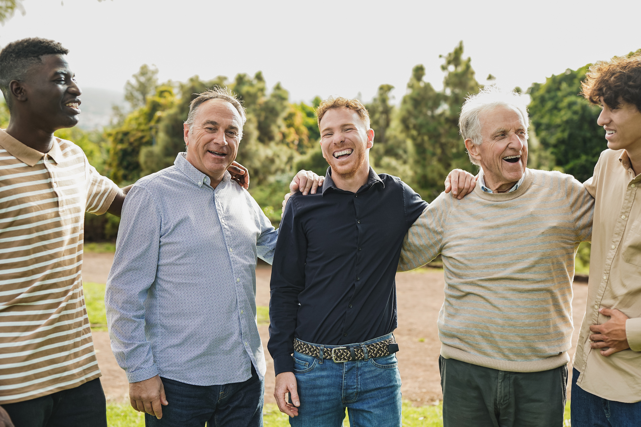 A group of men of different ages and ethnicities standing outside looking happy