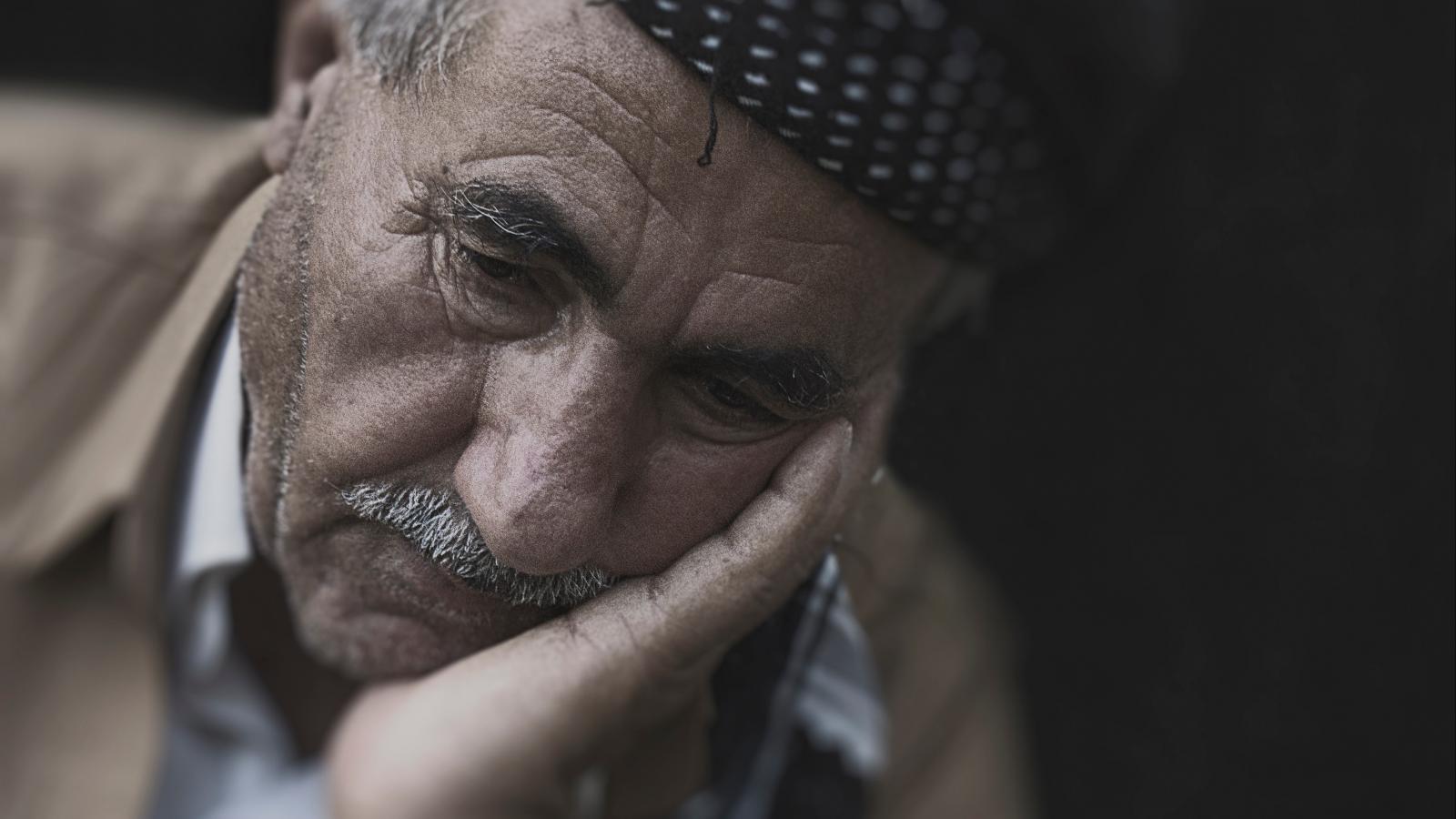 A sad older man sits with his head on one of his hands