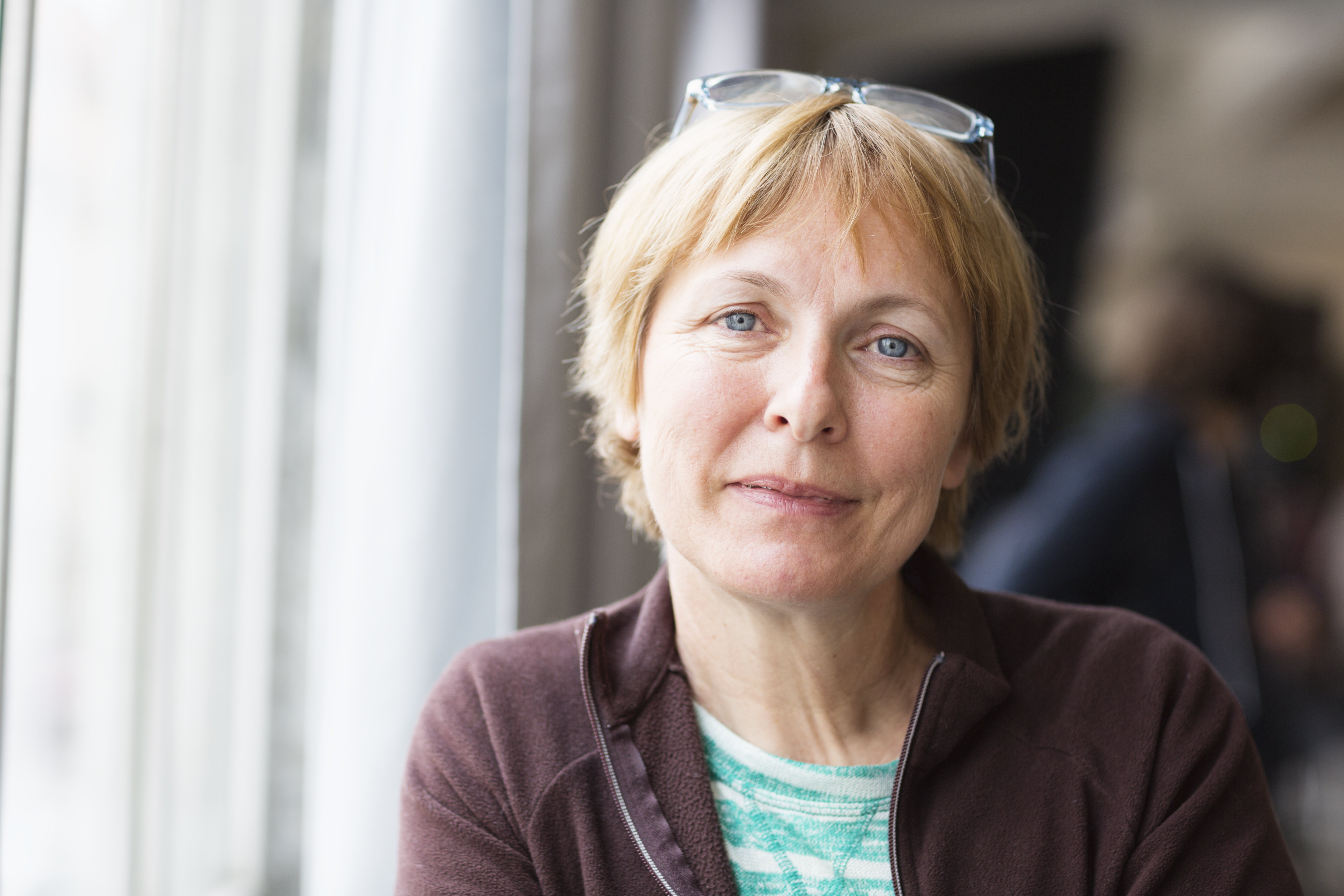 A middle aged woman with short blonde hair looks into the camera with a slight smile on her face