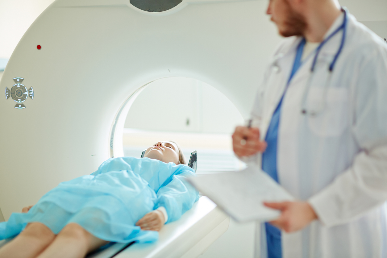 woman lying flat about to enter an MRI scanning machine, while a male doctor watches her