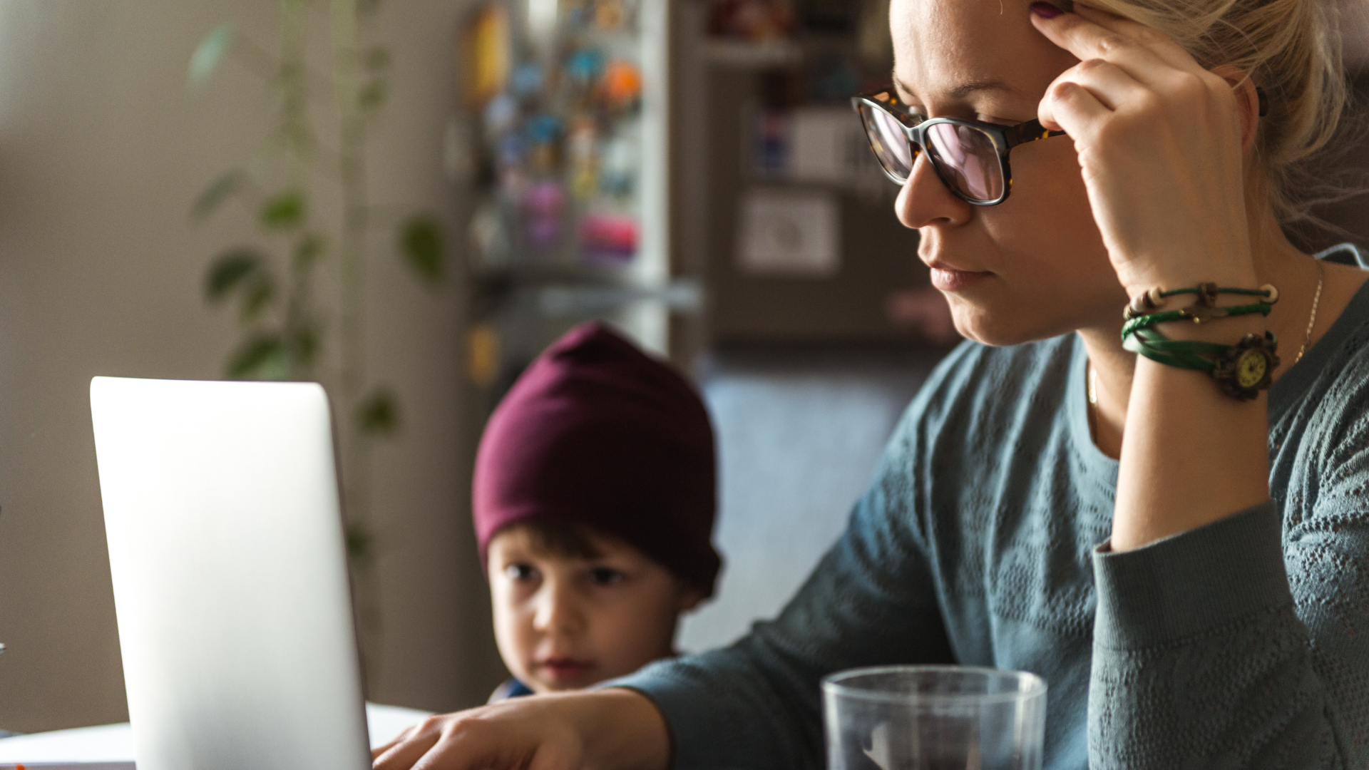 A mother using a laptop with her child in the background