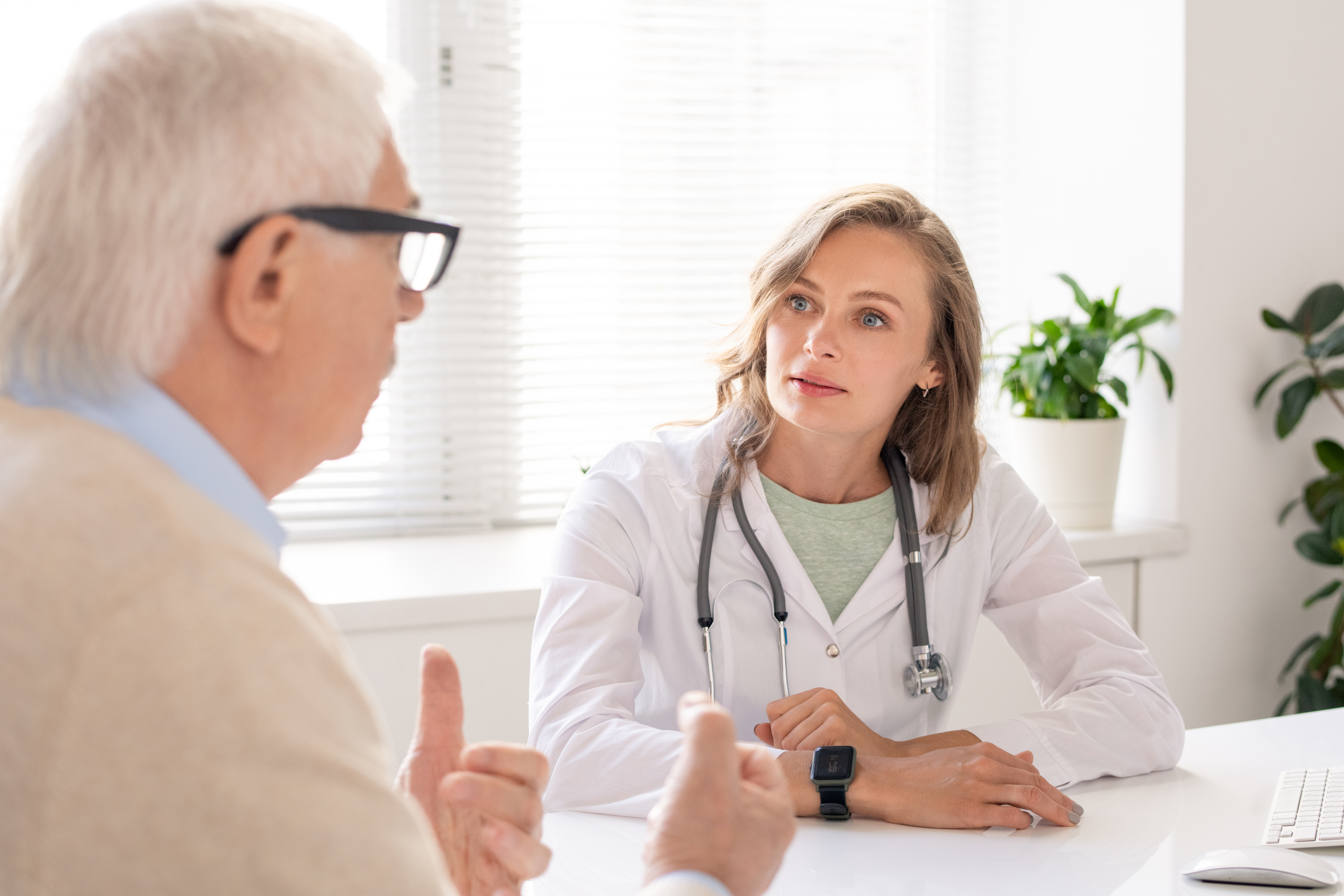An elderly man wearing glasses explains something to a young female doctor.