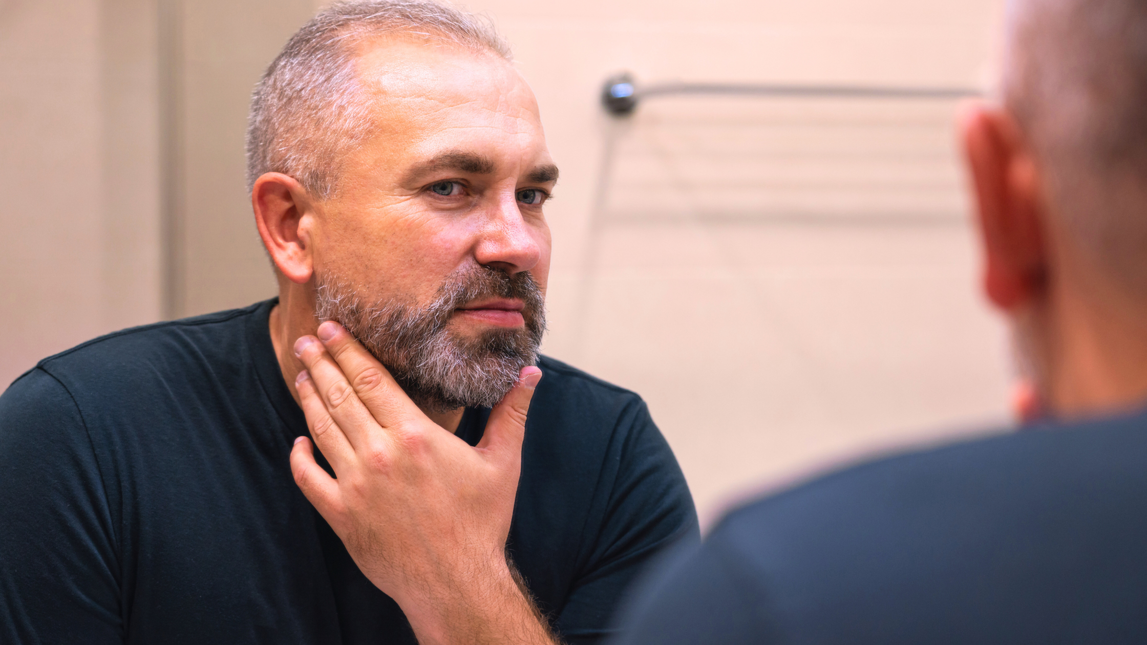 white middle-aged man looks at his jawline in the mirror