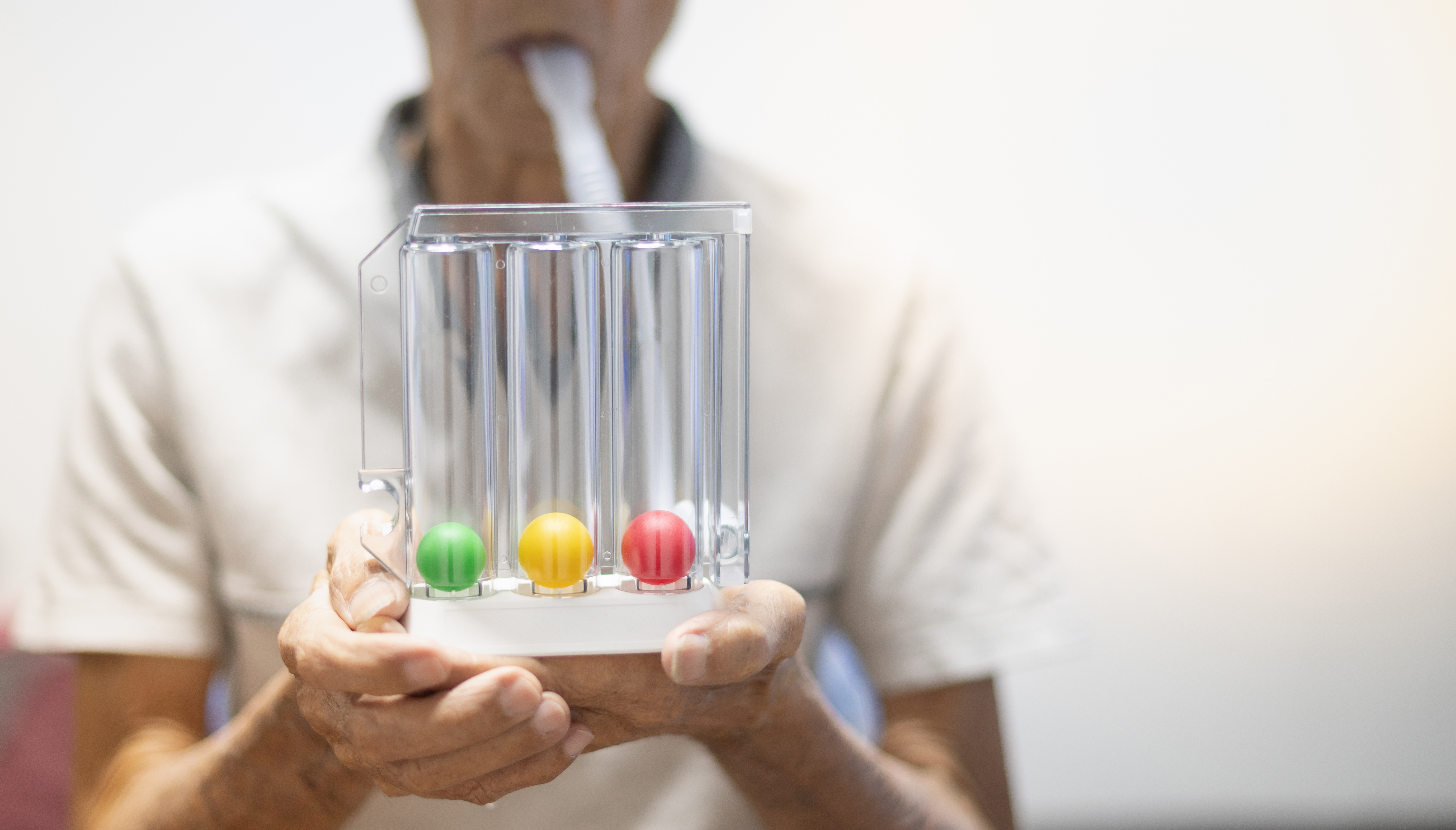 A patient blows into a tube leading to a plastic device with 3 clear cloumns, each with a coloured ball at the bottom