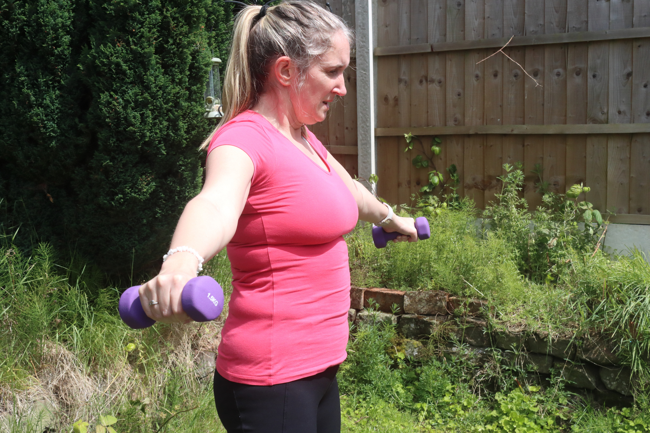 A lady in her garden doing an exercise with hand weights