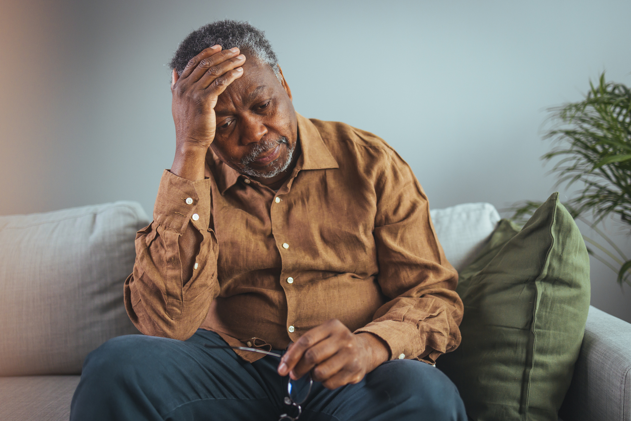 A Black man sitting on a sofa with his head in his hand, looking sad