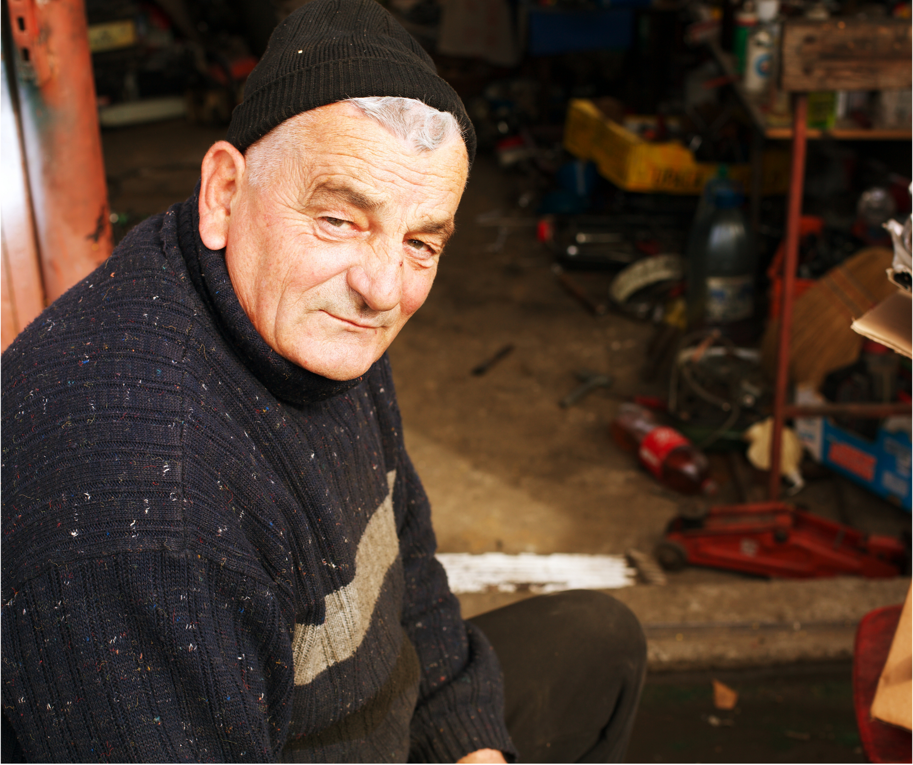 Older white Irish man woolen jumper at workplace with tools eyes to camera
