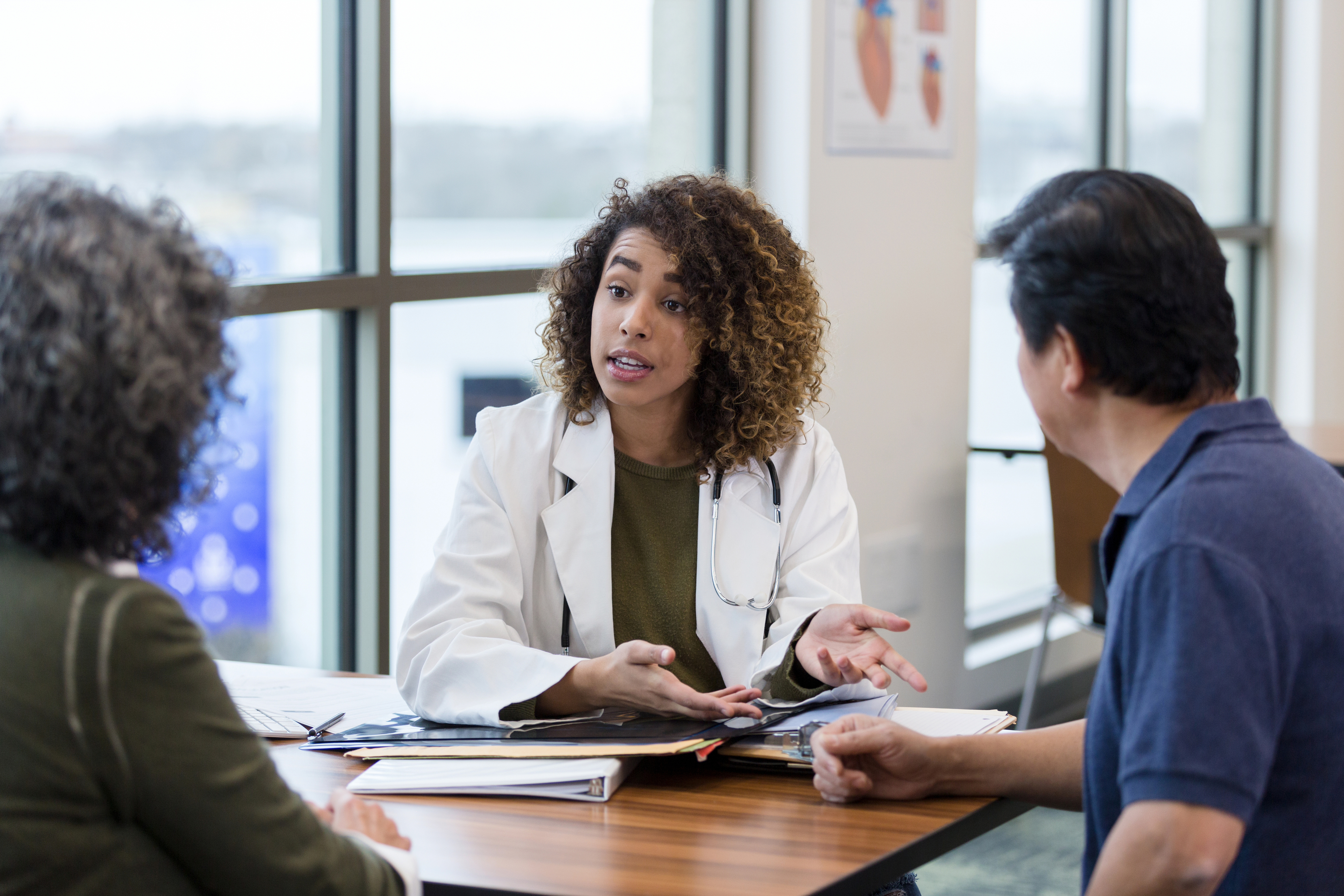 A mixed race female doctor in her 30s is talking to a Chinese lady and a Chinese man across a desk