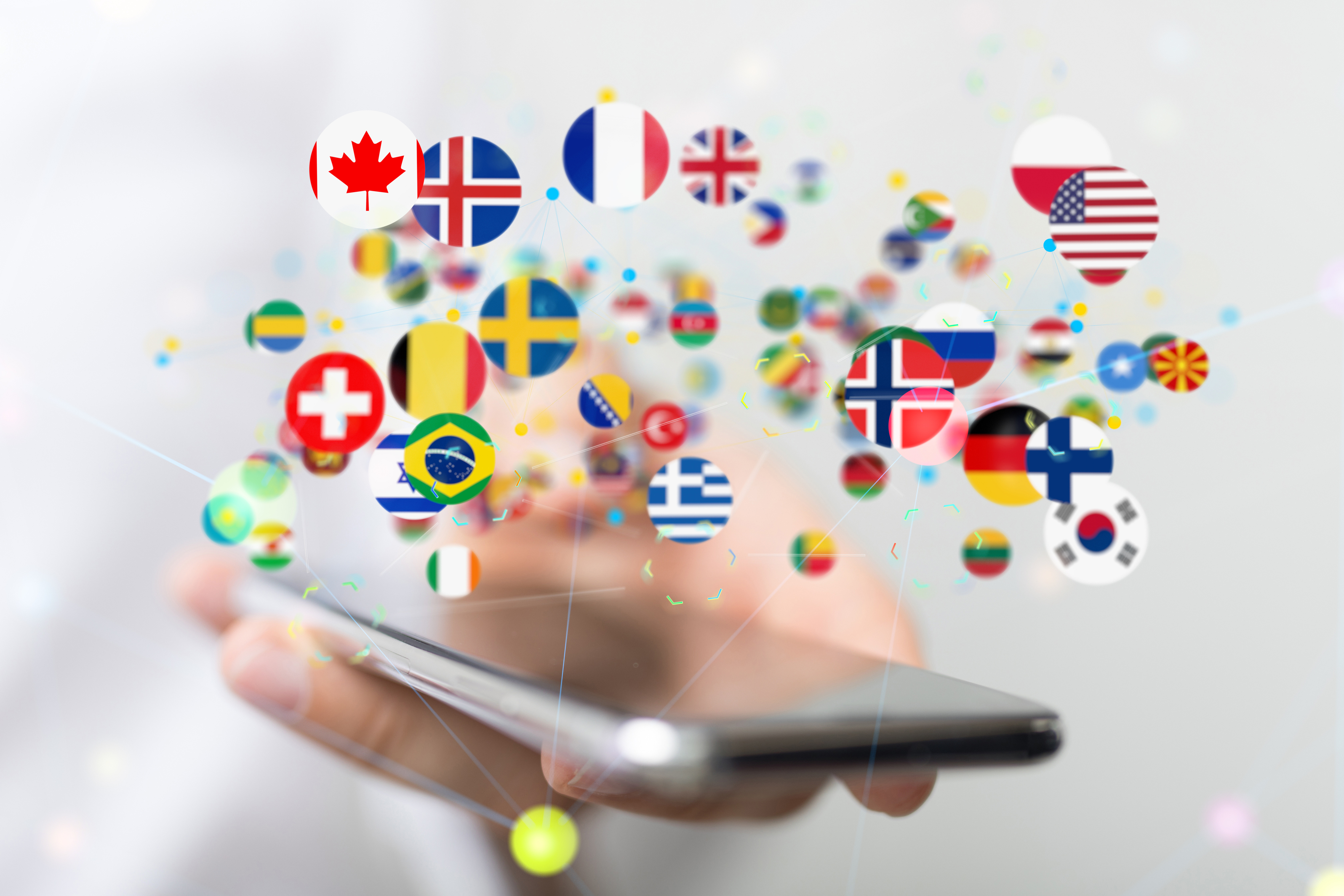A person holding a mobile phone. There are many flags from different countries coming from the phone