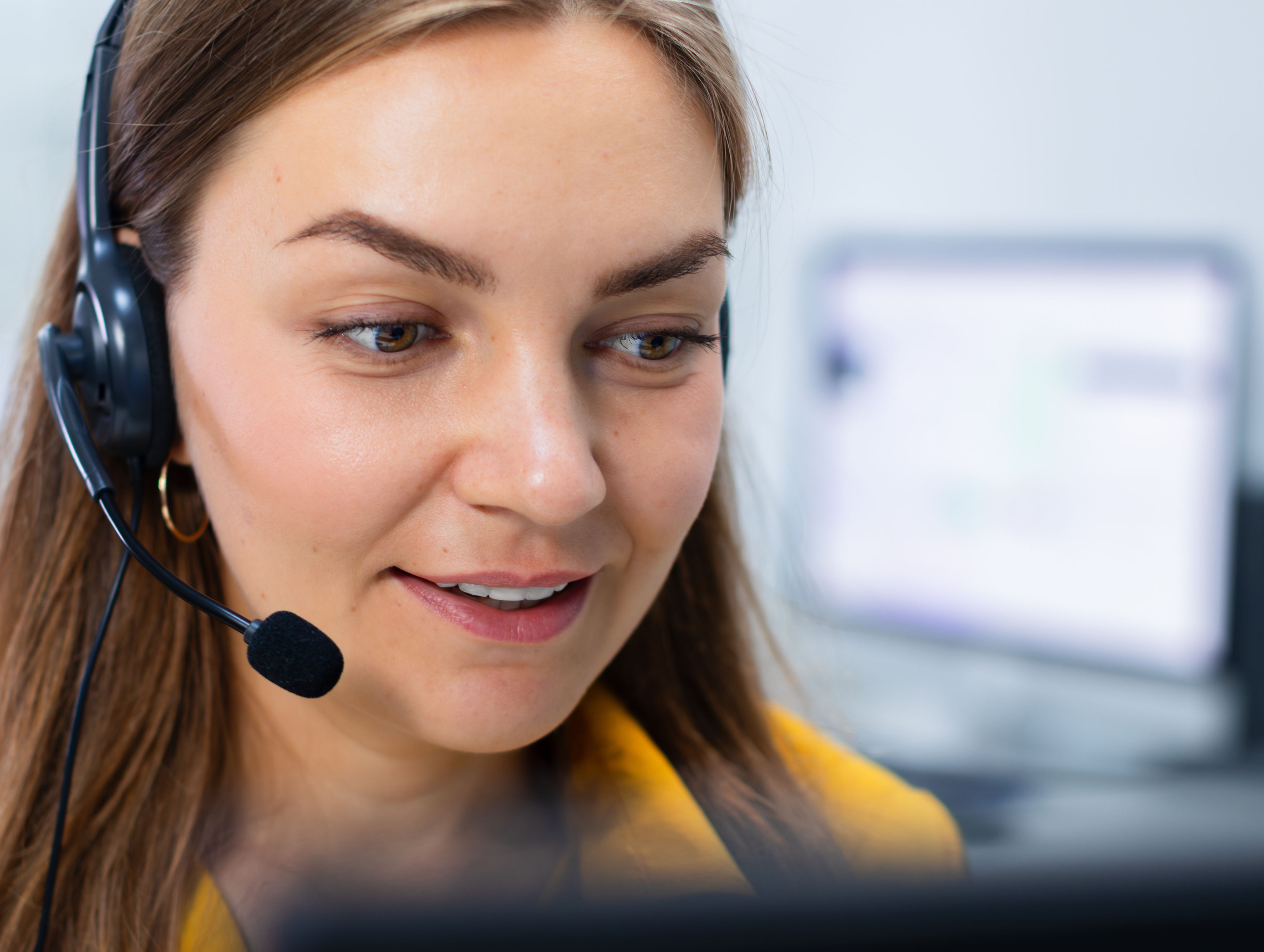 A lady in her thirties with long dark hair is talking into a telephone headset. She looks friendly and happy and is concentrating on the call.