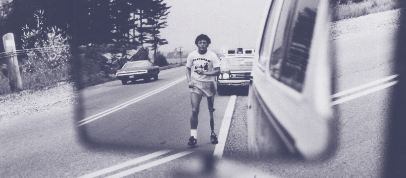 Young man with curly hair shown in a rearview mirror walking with one prostetic leg in a while T-shirt