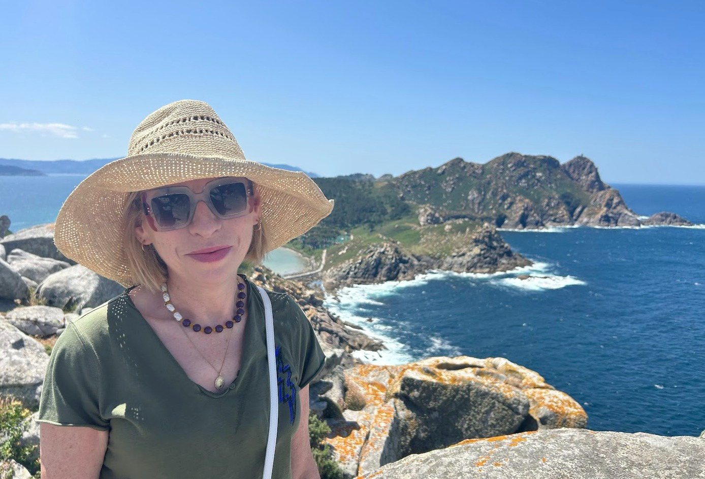 Fiona in sunglasses and a hat, with the sea and cliffs in the background