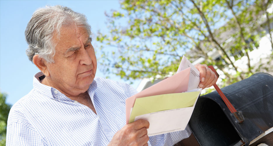 An older man looking at a letter with worry