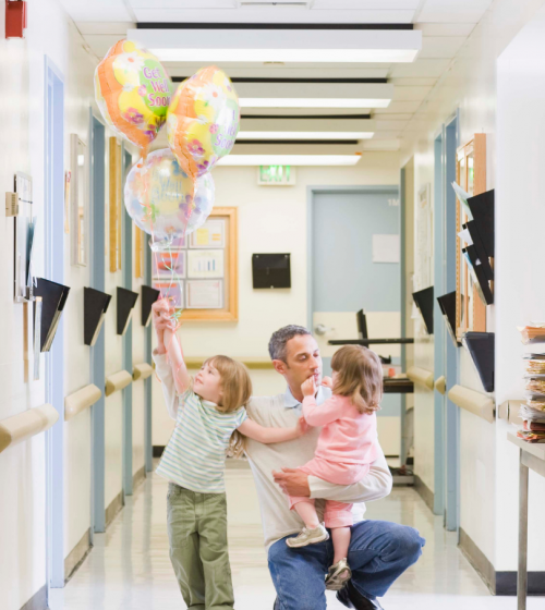 Parent and children in a hospital corridor holding balloons