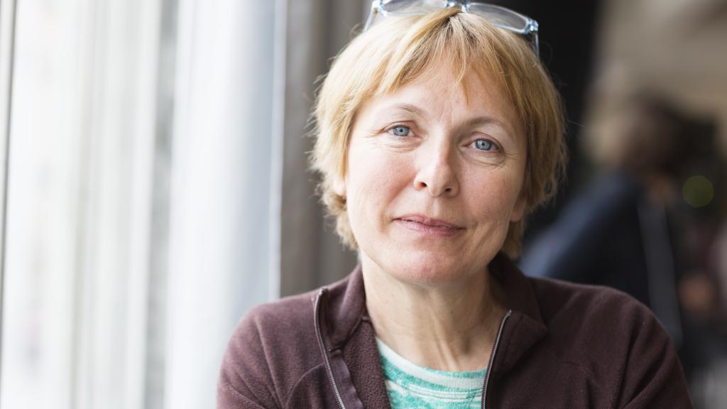 A middle aged woman with short blonde hair looks into the camera with a slight smile on her face