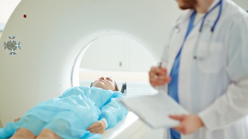 woman lying flat about to enter an MRI scanning machine, while a male doctor watches her