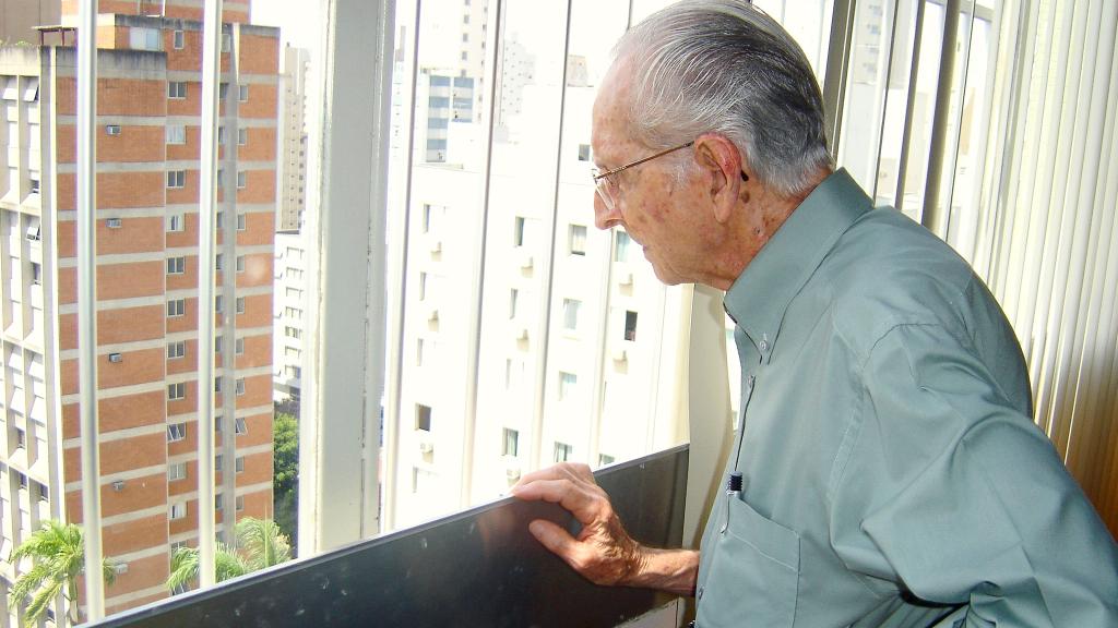 An elderly man looks out of the window of his multi-story flat
