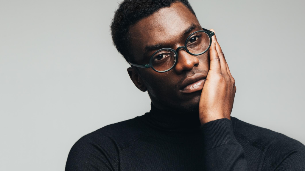 Young black man wearing glasses holding his face and looking worried