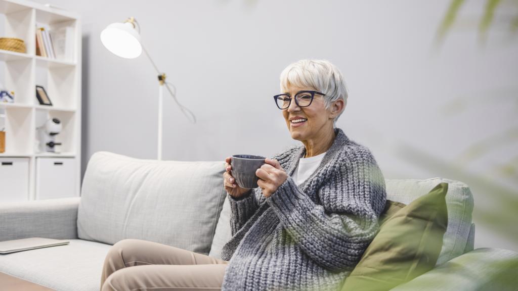 older woman indoors with coffee and warm jumper