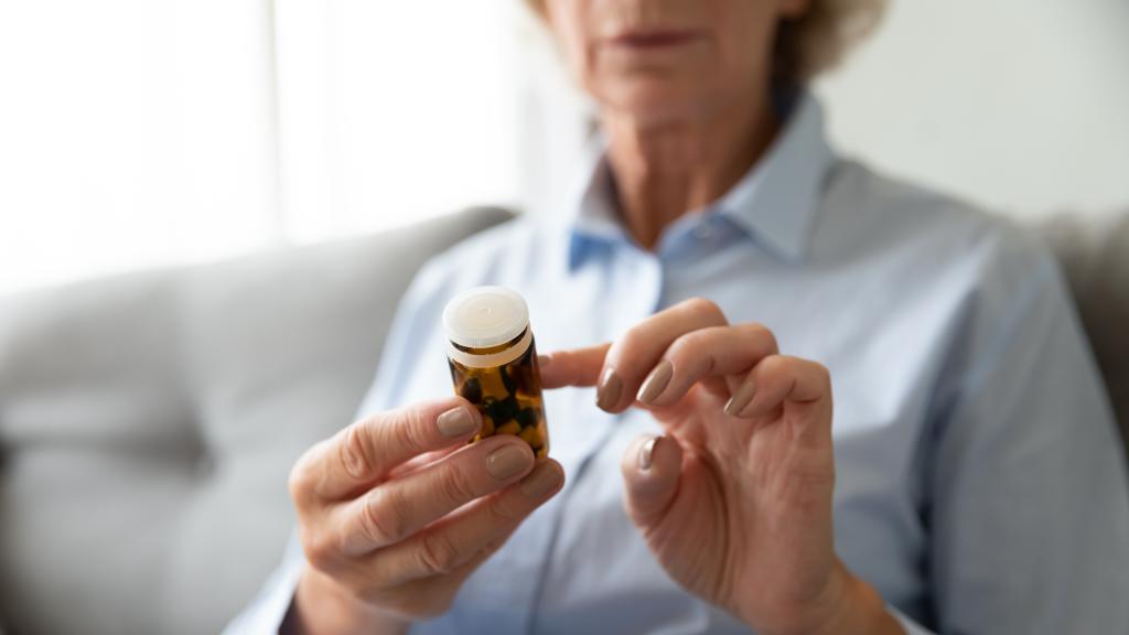 A woman in her sixties wearing glasses carefully examining the label on a medicine bottle