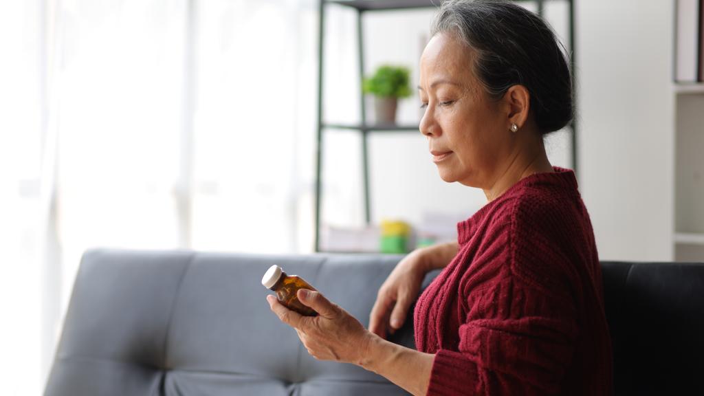 An Asian middle-aged woman looking at a bottle of pills