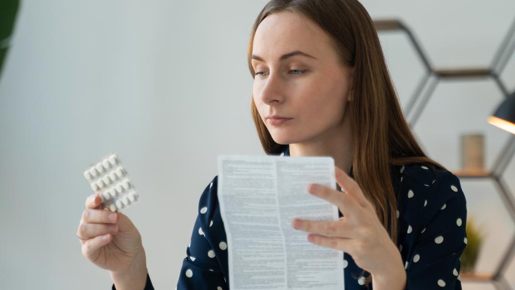 A woman in her thirties holding a pack of tablets and reading the instruction sheet