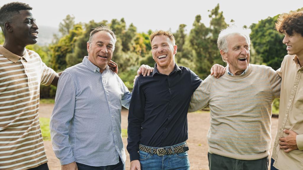 A group of men of different ages and ethnicities standing outside looking happy