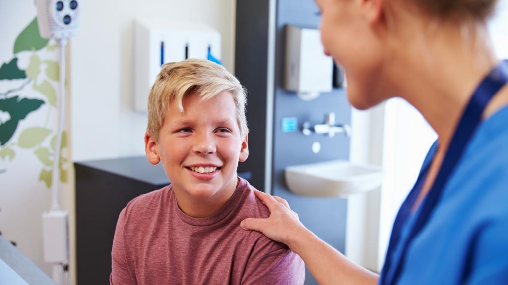 Photo of a smiling teenage boy talking to a doctor