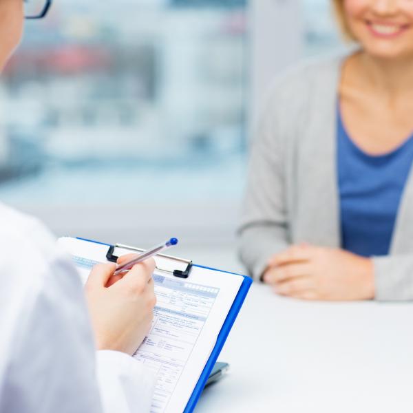 Woman talking to a doctor. The doctor is holding a clipboard.