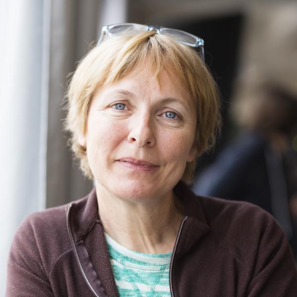 A middle aged woman with short blonde hair looks into the camera with a slight smile on her face