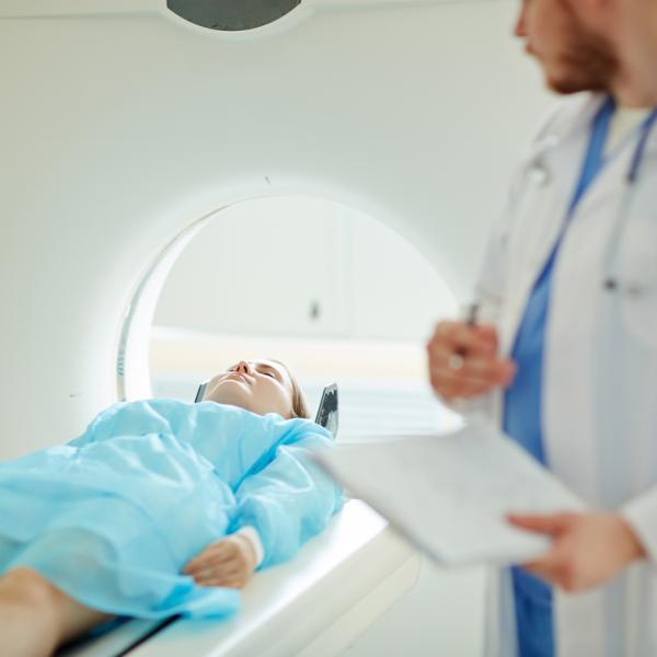 woman lying flat about to enter an MRI scanning machine, while a male doctor watches her