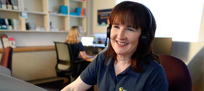 Nurse in navy t-shirt sitting at computer with headset on smiling 
