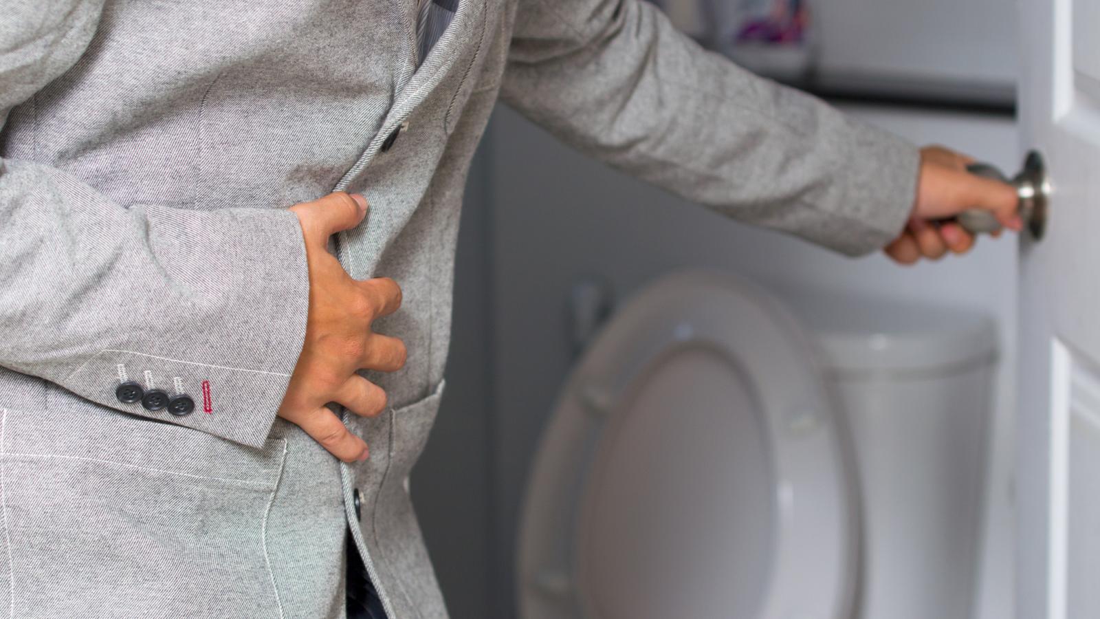 A man wearing a suit and holding his tummy opening the door to the toilet