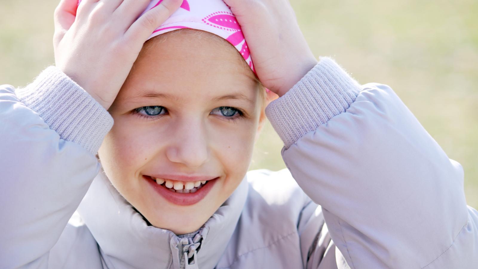 A smiling girl holding her bandana, which covers her bald head