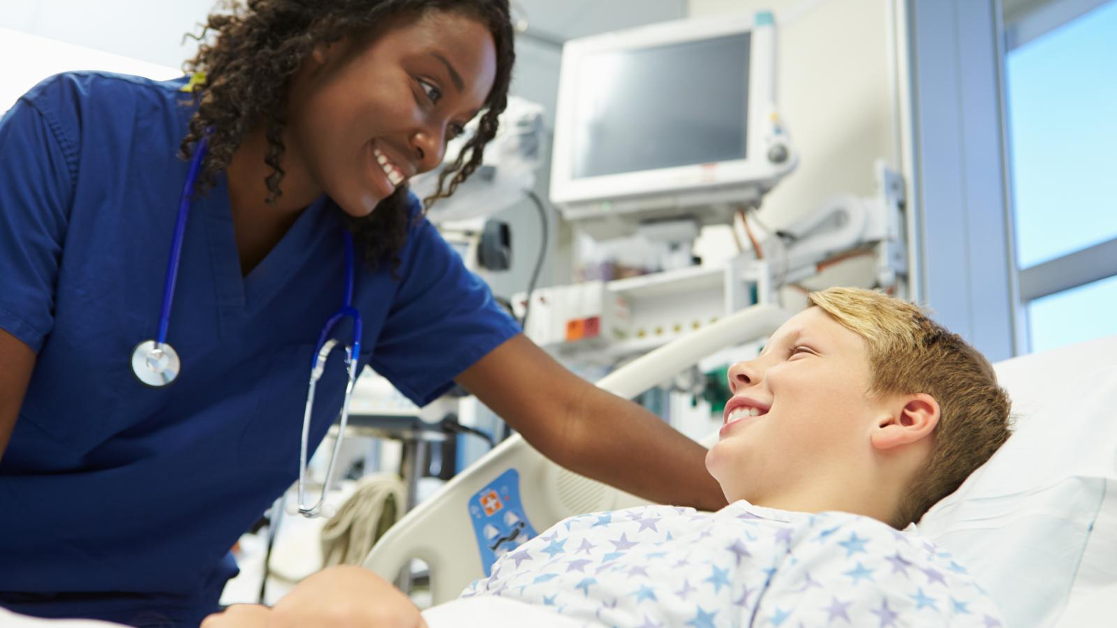 A boy in a hospital bed smiling at his nurse