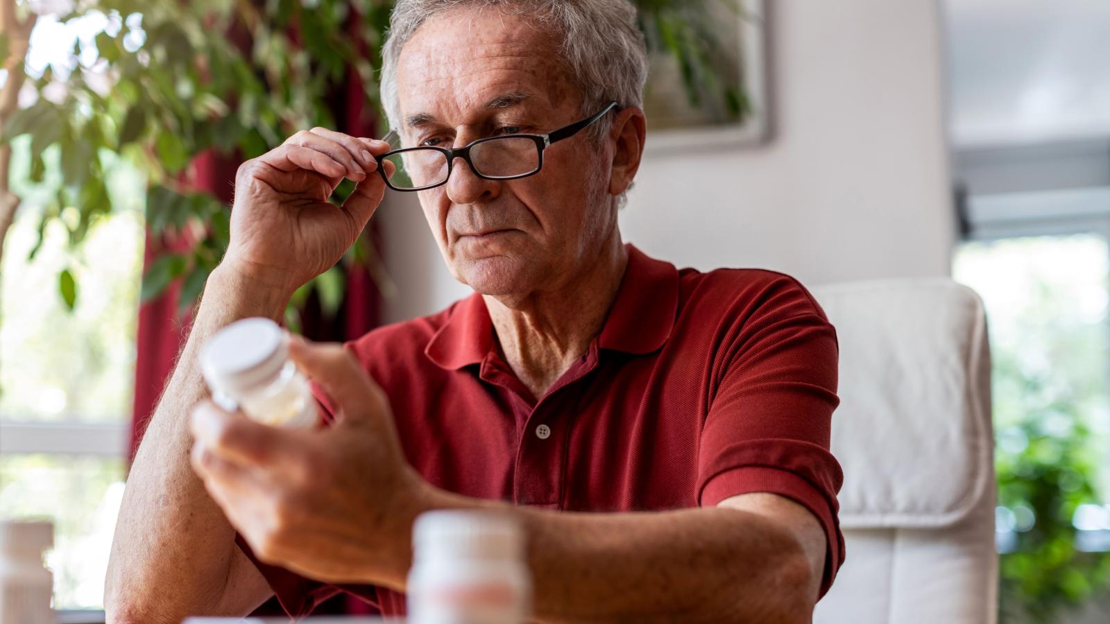 A man in his sixties wearing glasses carefully examining the label on a medicine bottle
