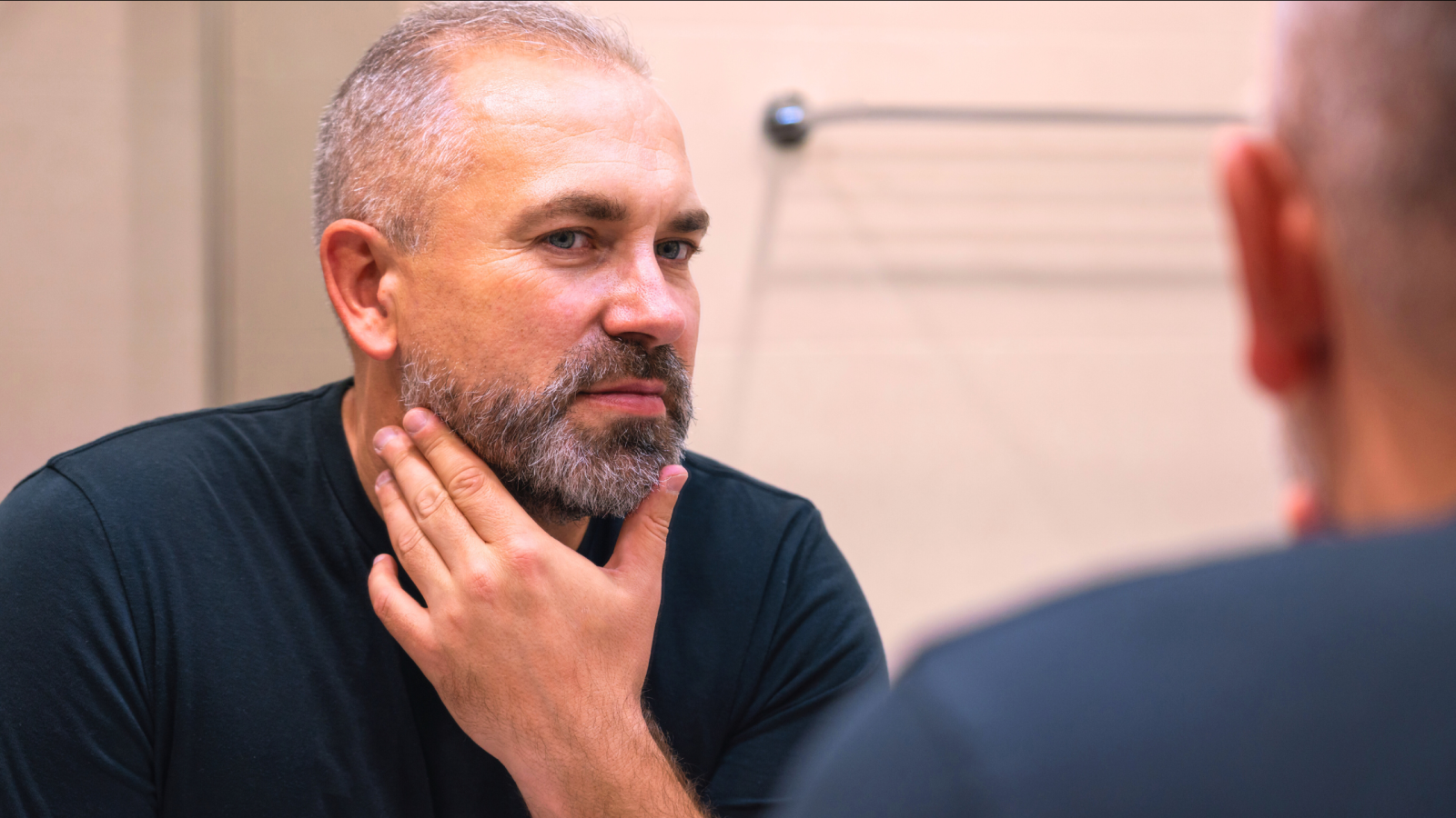 white middle-aged man looks at his jawline in the mirror