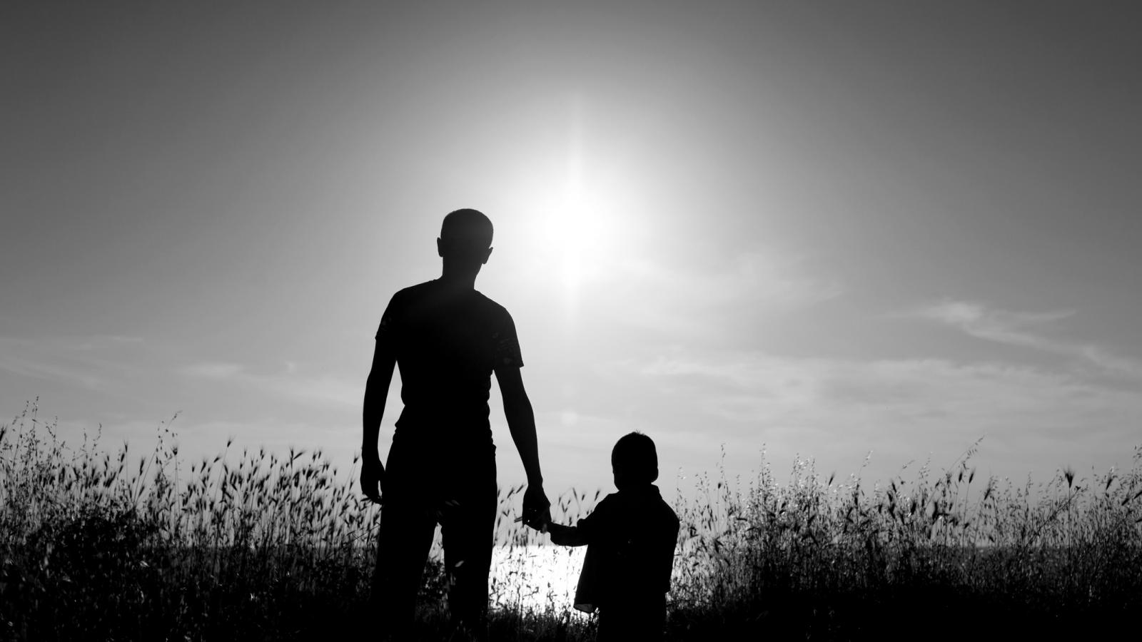 Father and child standing against a sunset