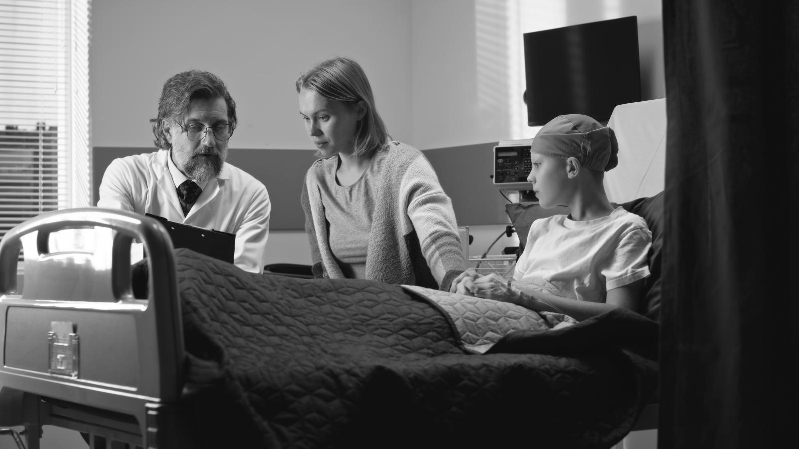A doctor explains to a mother and a boy with cancer, who is in a hospital bed