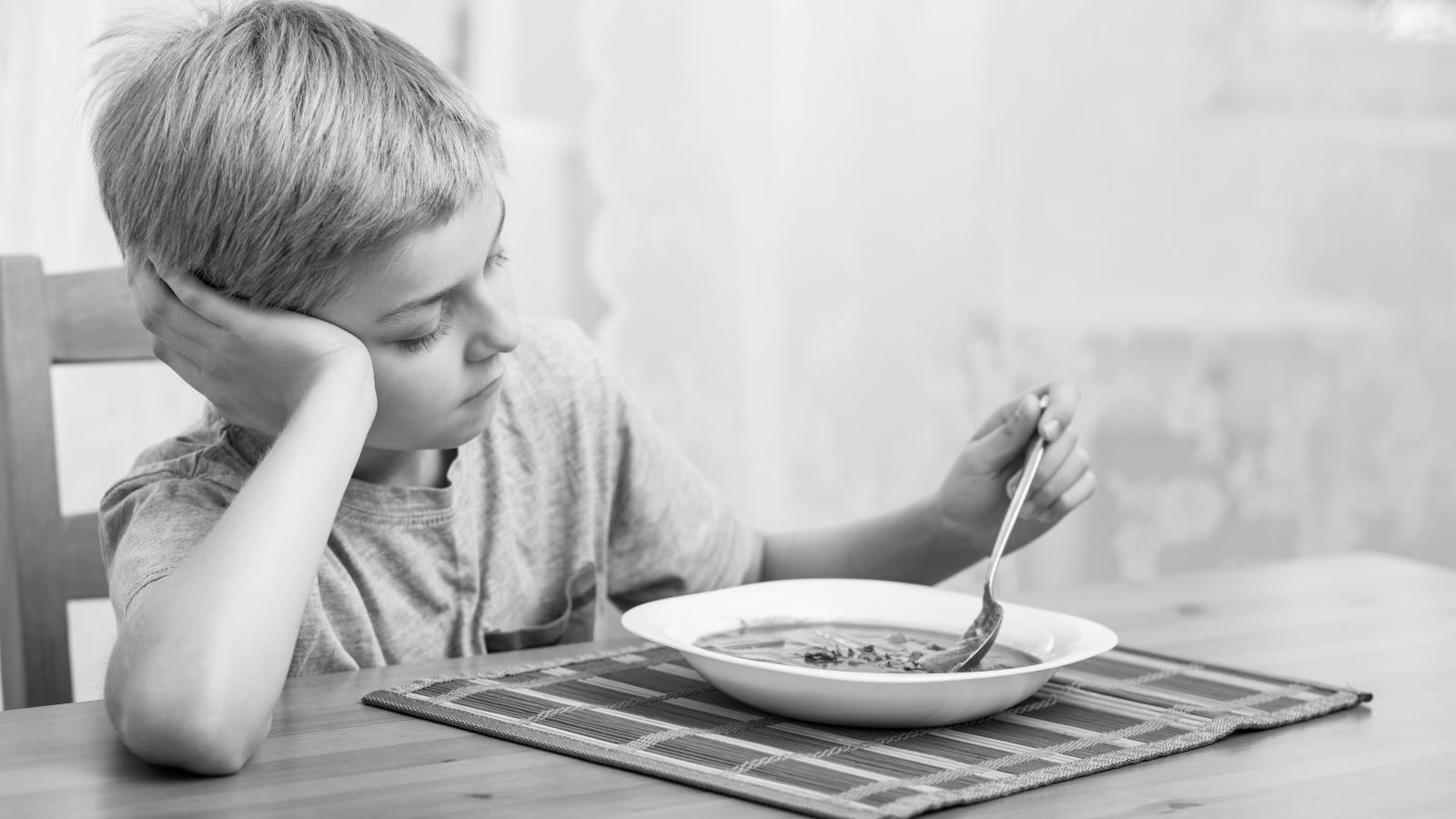 A boy with a bowl of soup looking sad