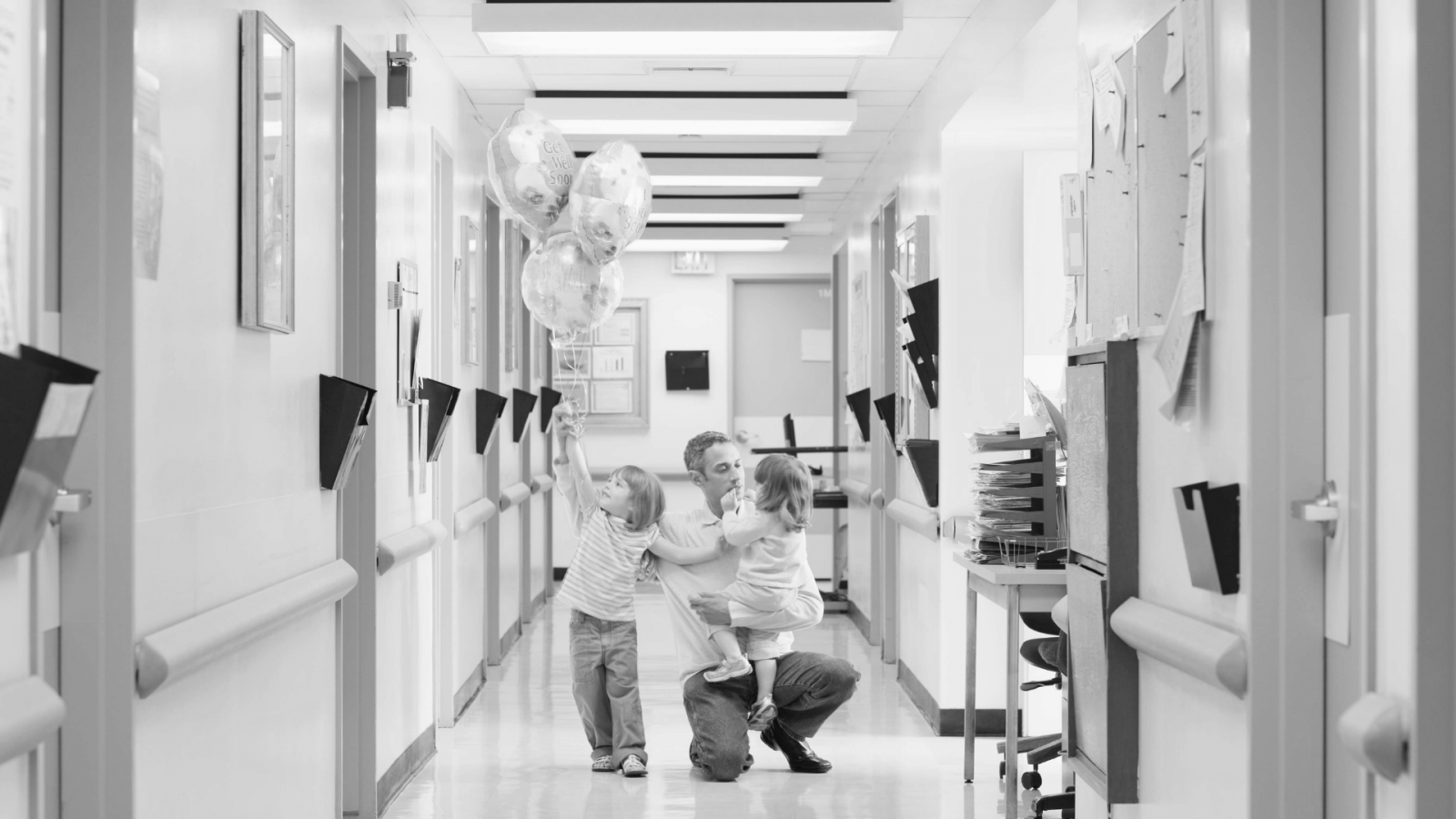 Parent and children in a hospital corridor holding balloons